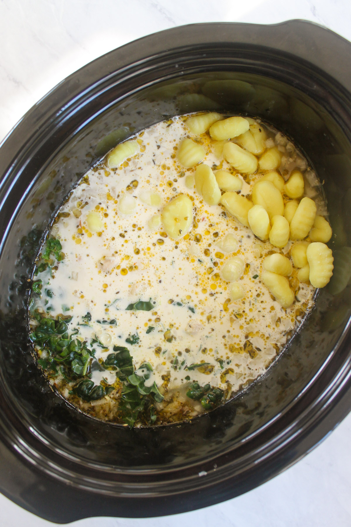 Gnocchi, kale and cream added to chicken soup in a slow cooker.