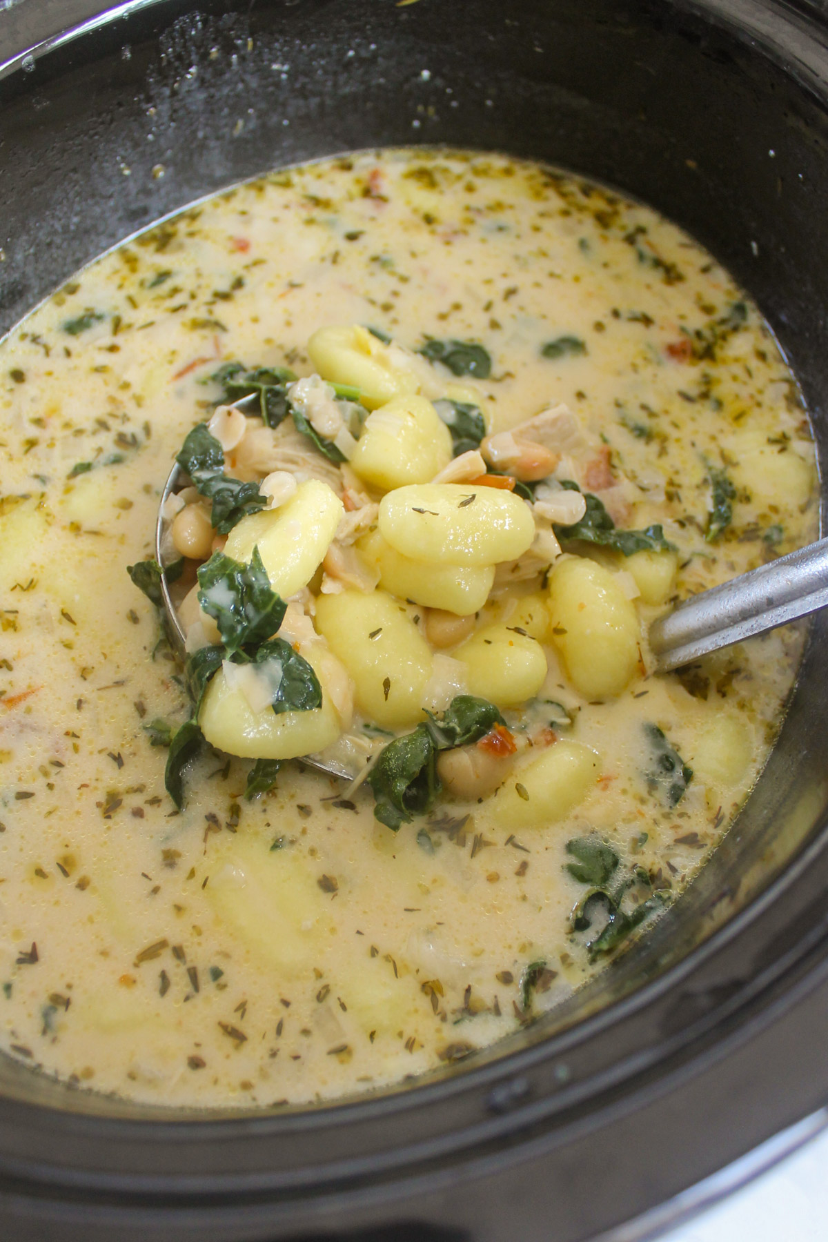 Chicken Gnocchi White Bean Soup in a slow cooker with a ladle.