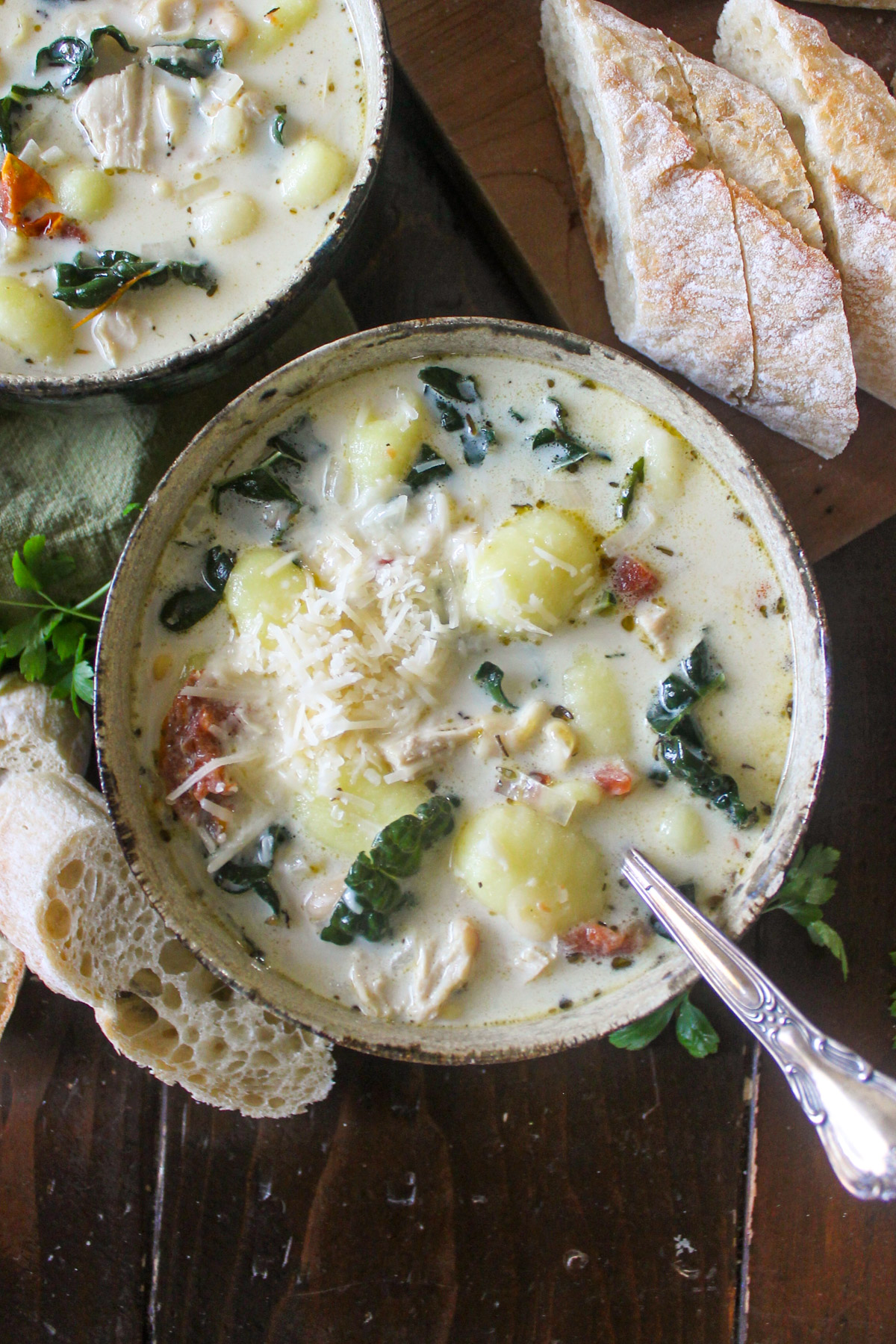 A bowl of chicken gnocchi soup with kale and Parmesan cheese.