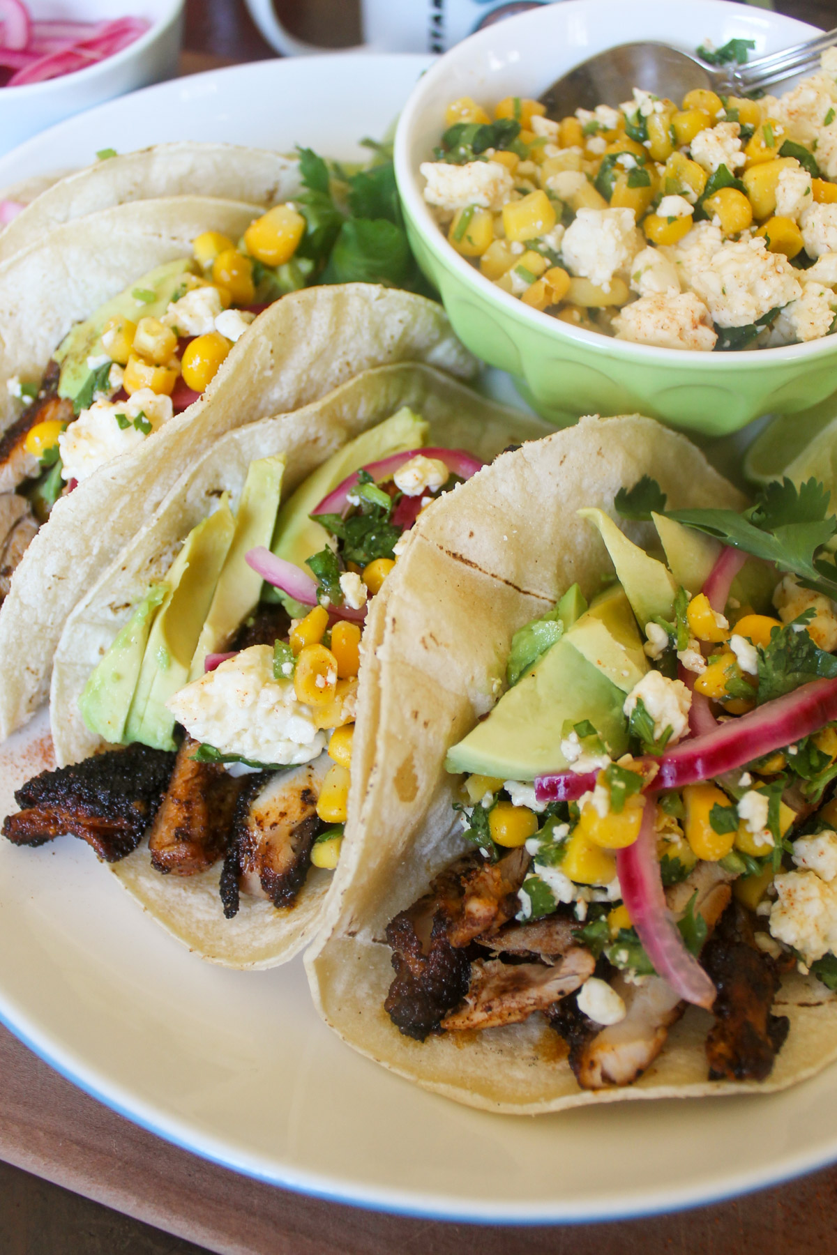 Blackened chicken tacos with corn salsa and avocado slices.