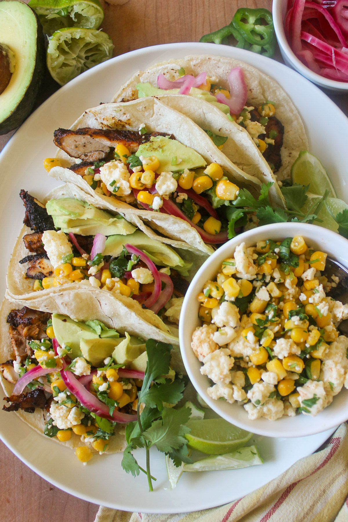 Blackened chicken tacos on a plate with a bowl of Cotija cheese corn salsa.