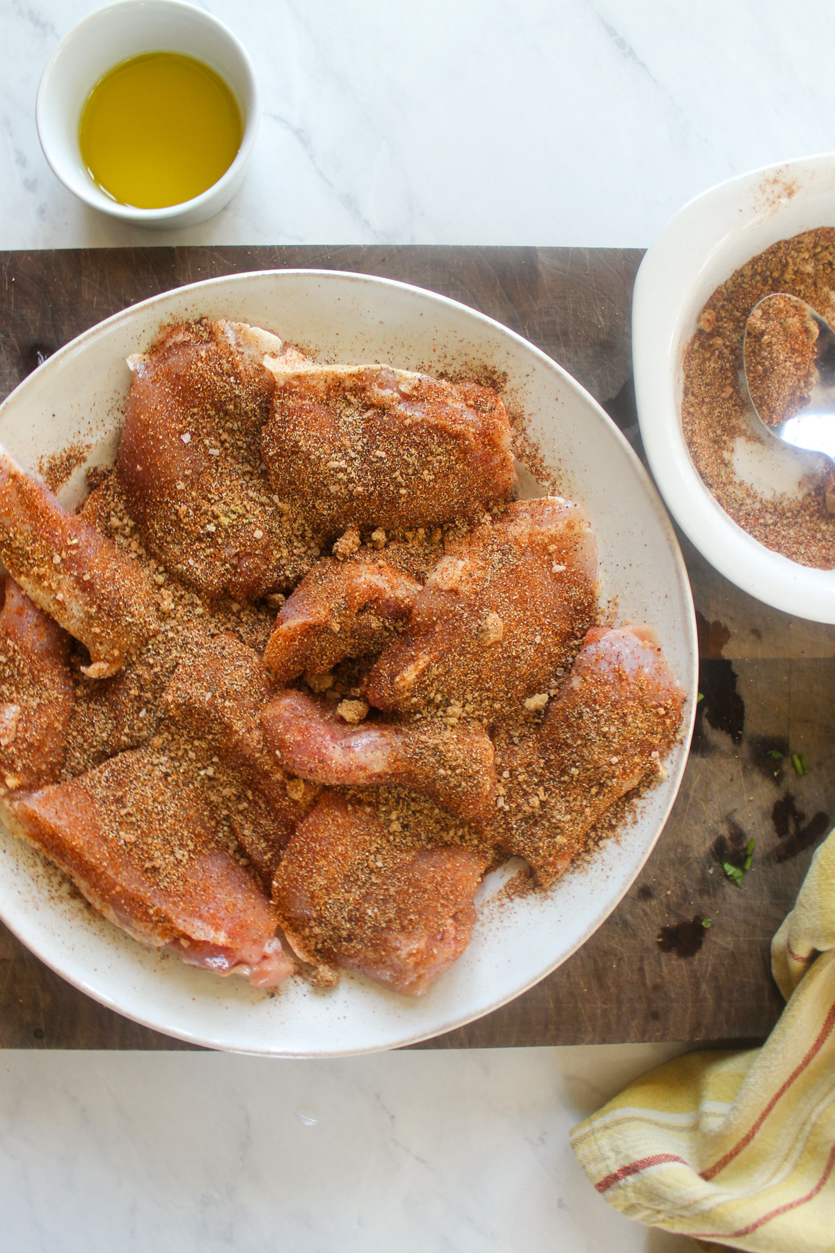 Raw chicken thighs on a plate heavily seasoned with blackening spices.