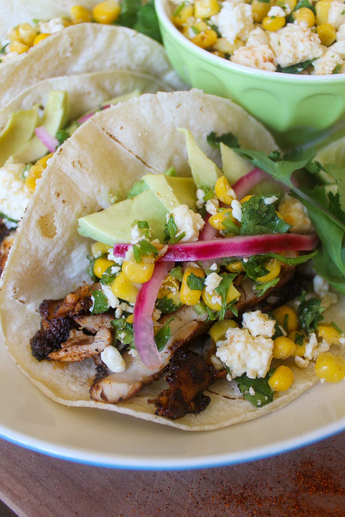 A soft taco with blackened chicken, corn, Cotija cheese, avocado slices, cilantro and pickled red onions.