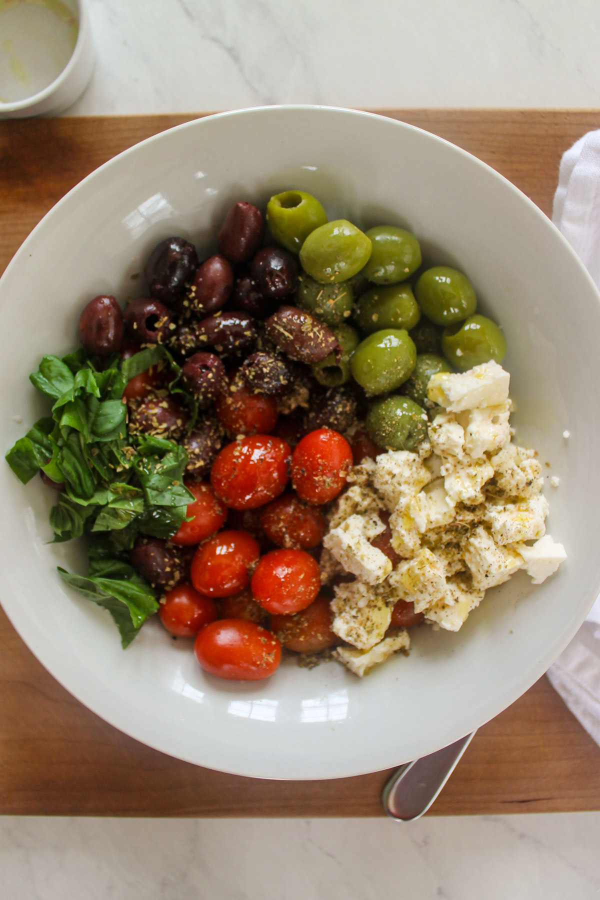 Ingredients in a white bowl with olives, tomato, cheese and basil with oregano.