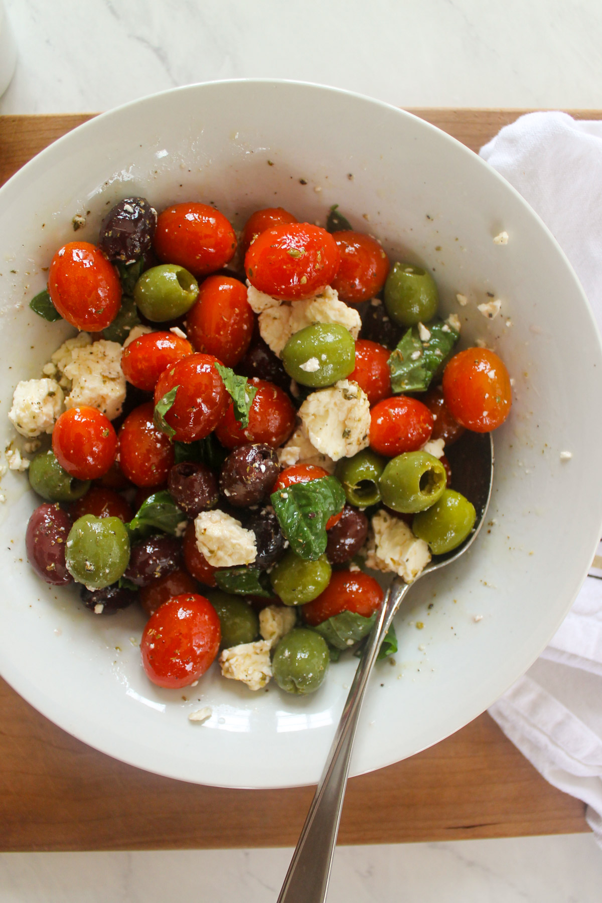 A mixing bowl with olives, tomato, feta cheese, basil and vinaigrette.