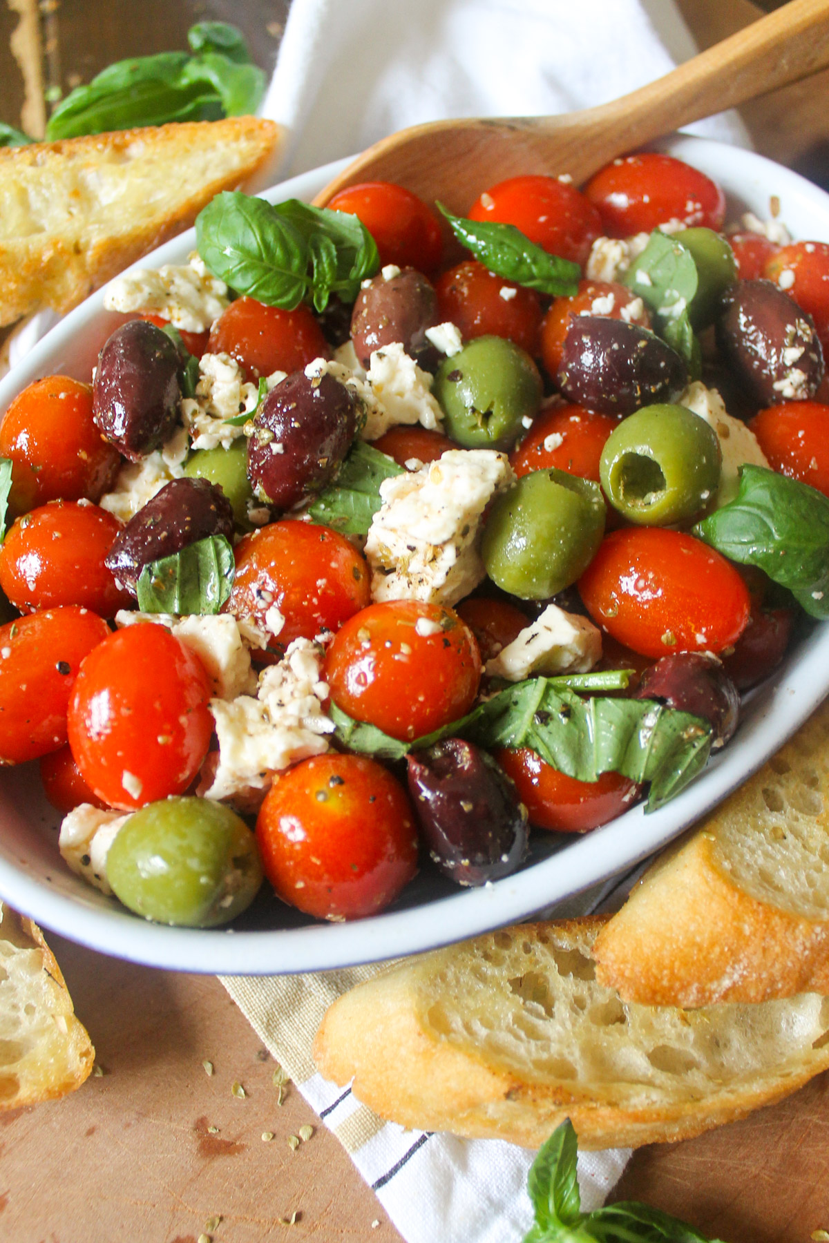 A serving dish of marinated olives with feta cheese and cherry tomatoes.