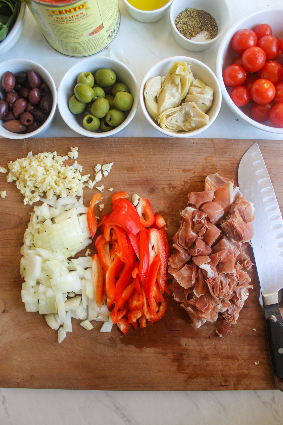 Chopped onion, red bell pepper and prosciutto on a cutting board.