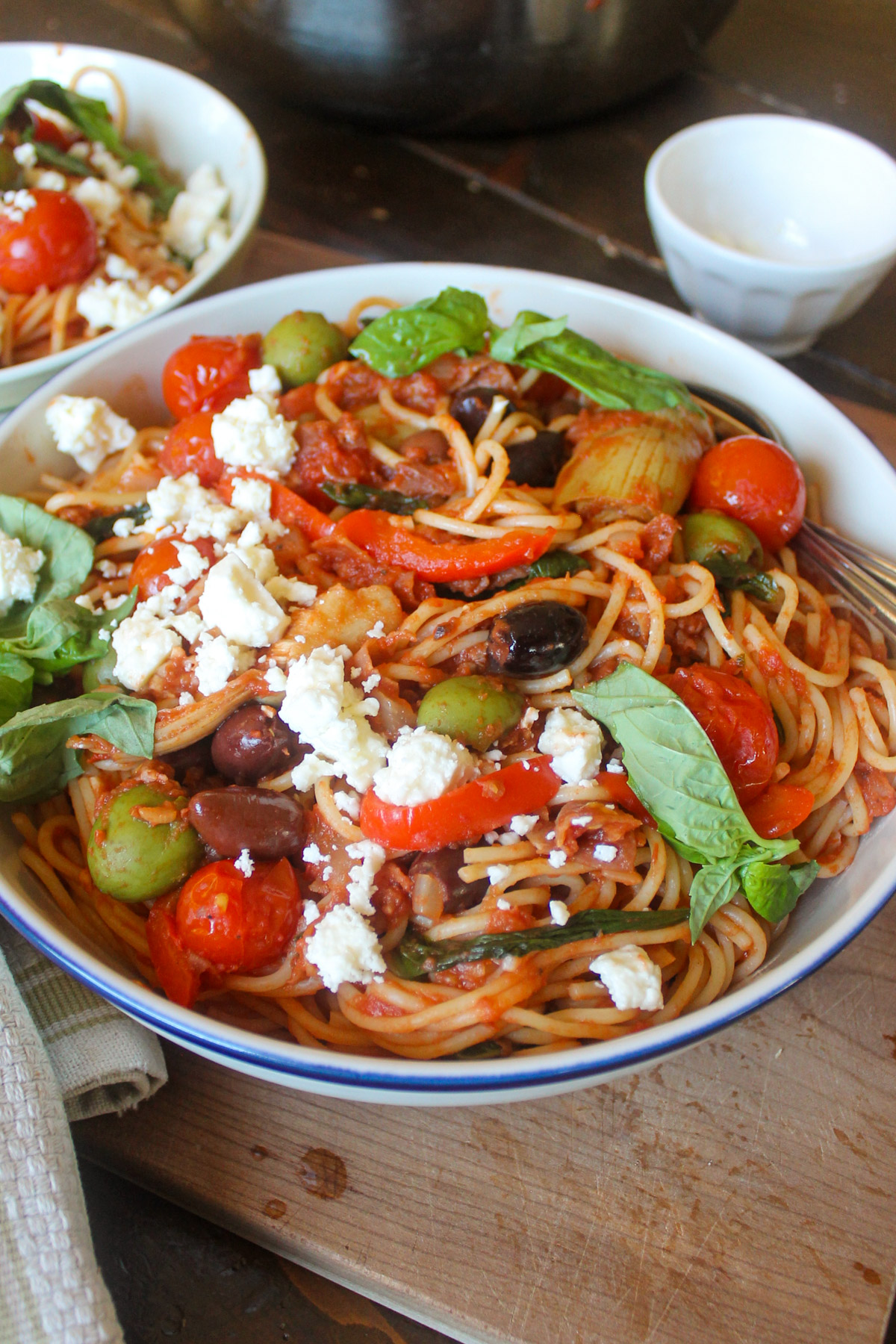 A serving bowl of spaghetti with prosciutto tomato sauce with olives and feta cheese.