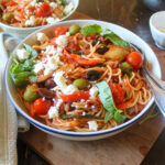 A bowl of spaghetti with prosciutto, olives, and basil tomato sauce.