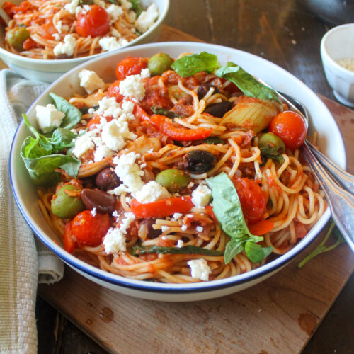 A bowl of spaghetti with prosciutto, olives, and basil tomato sauce.