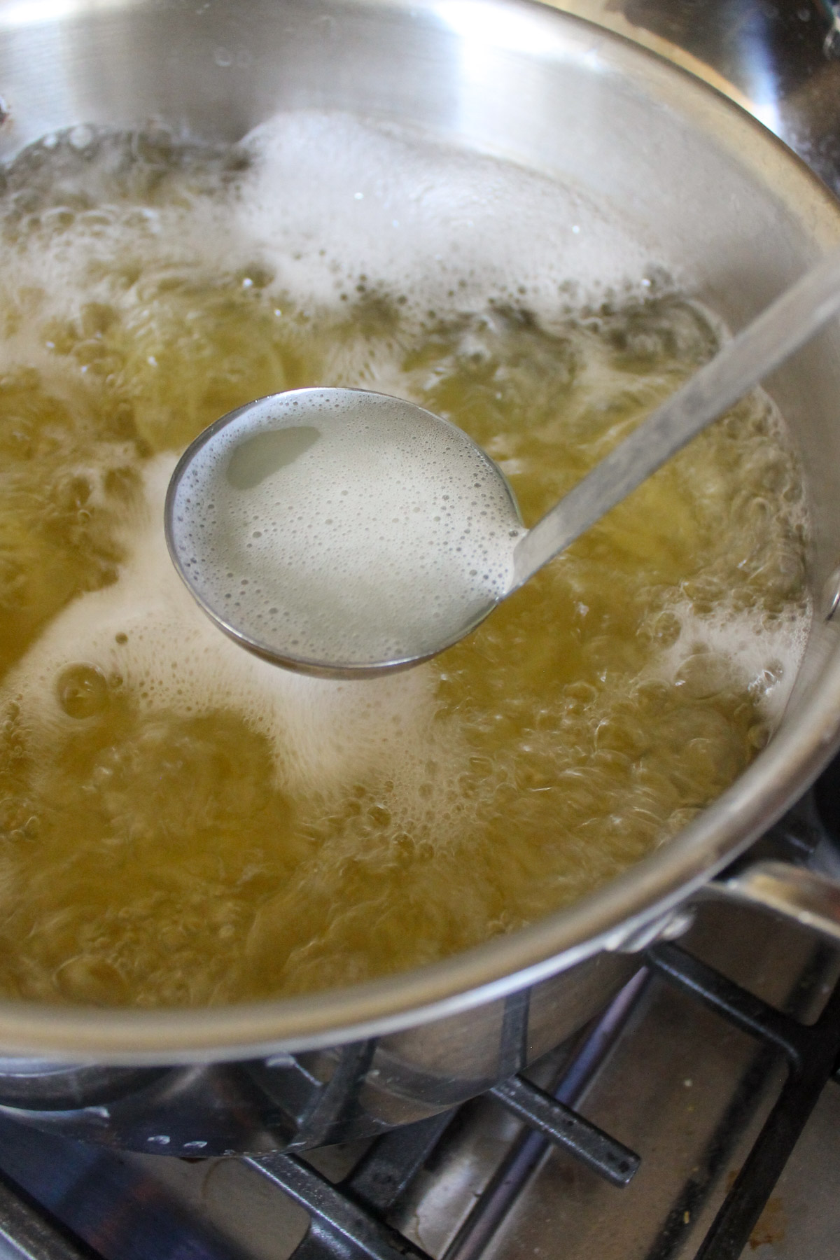 A ladle reserving starchy pasta cooking water from a boiling pot.