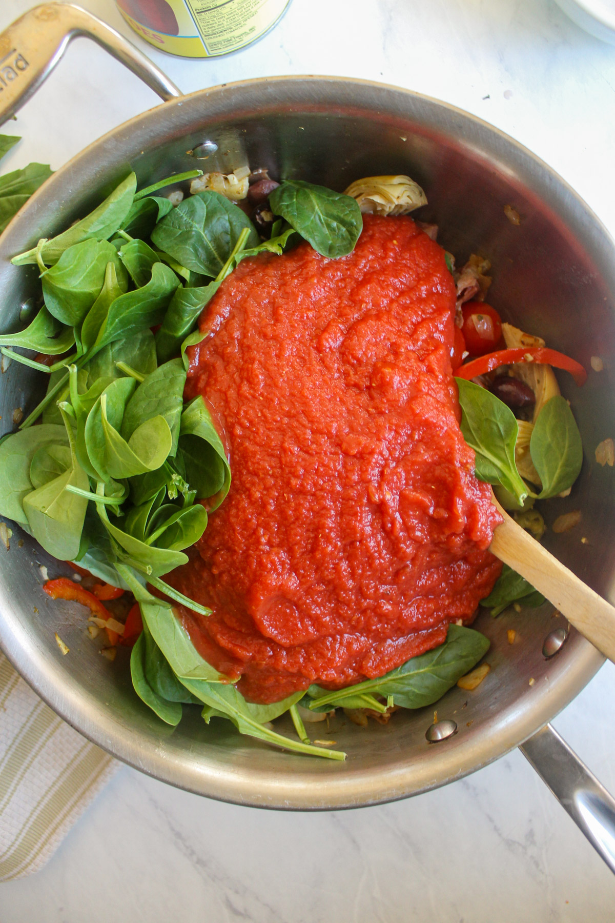 Adding fresh spinach and crushed tomato to a skillet.