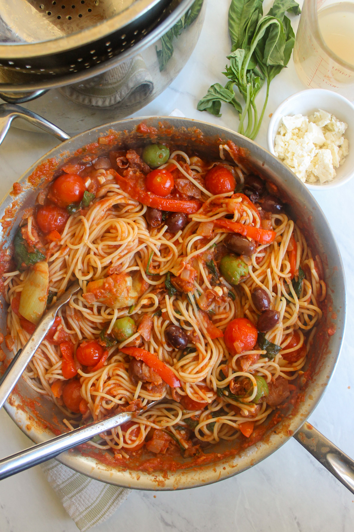 Prosciutto Olive Tomato Sauce tossing with spaghetti in a skillet.