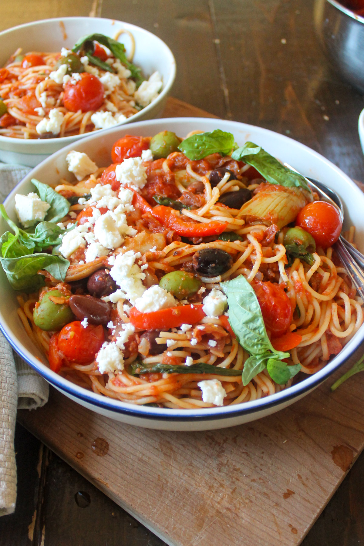 A serving bowl of spaghetti with prosciutto tomato sauce with olives and feta cheese.