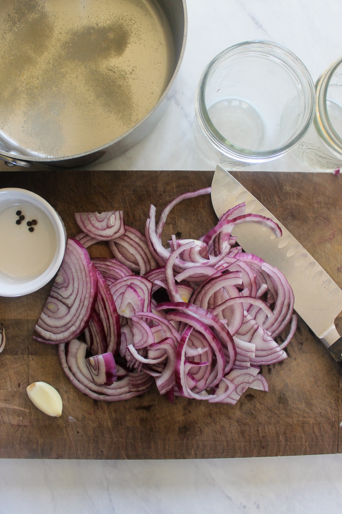 Red onion slices on a cutting board with a saucepan of vinegar brine.