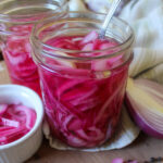 Two pink pint jars of pickled red onions.