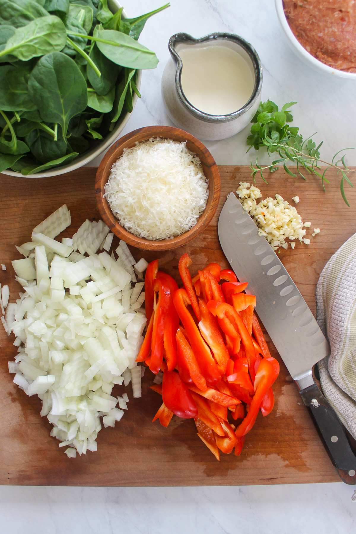 Chopped onions, peppers and garlic on a cutting board with spinach and Parmesan.