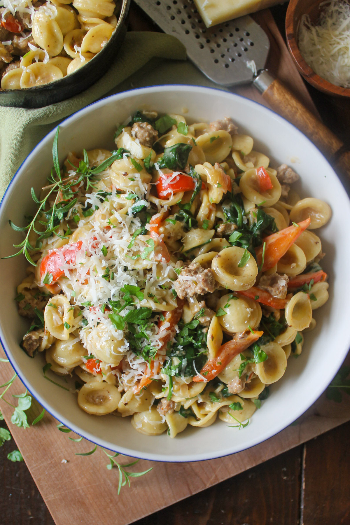 A bowl of pasta with sausage, peppers, spinach and Parmesan cheese.