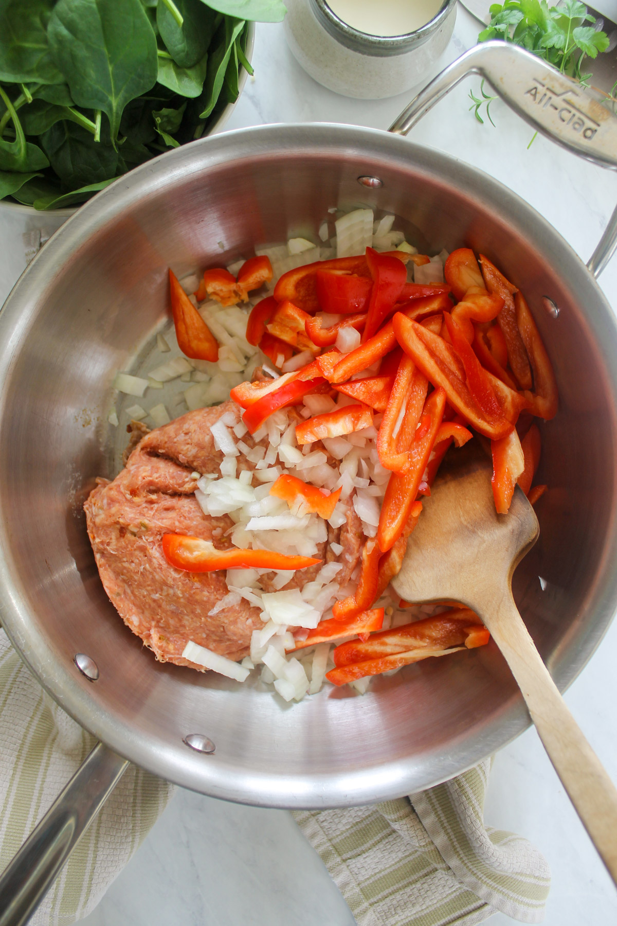 Cooking raw sausage, onions, and red bell peppers in a skillet.