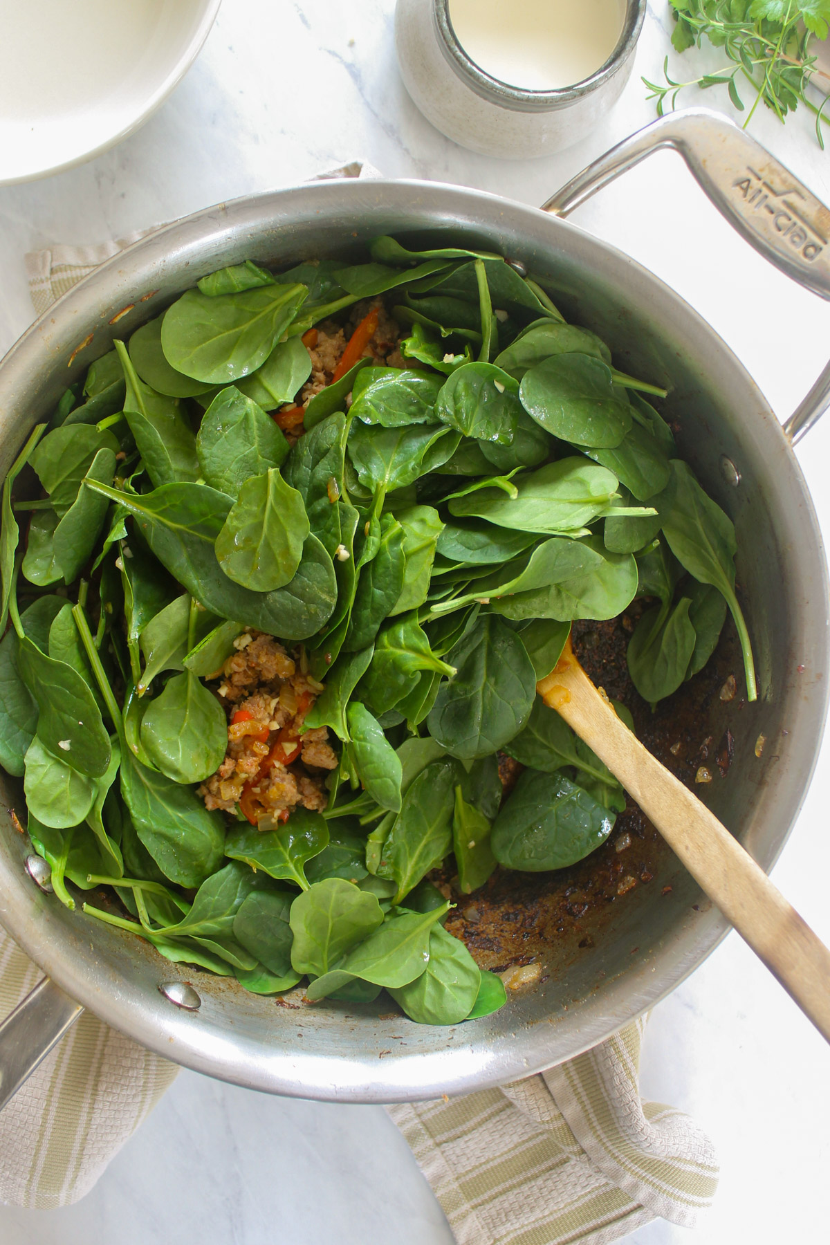 Adding fresh baby spinach to a skillet.