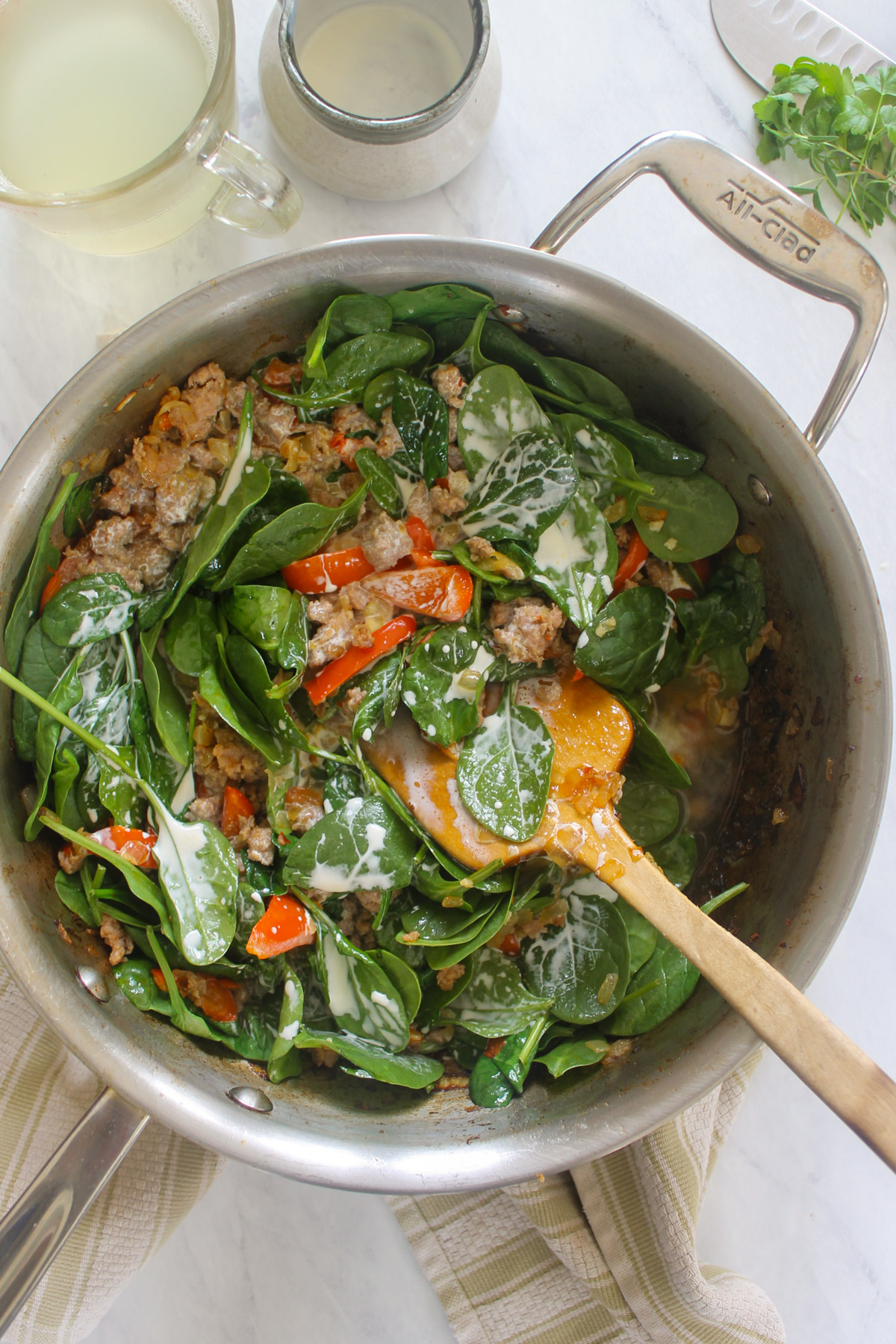 Adding cream to a skillet with spinach, sausage and peppers.