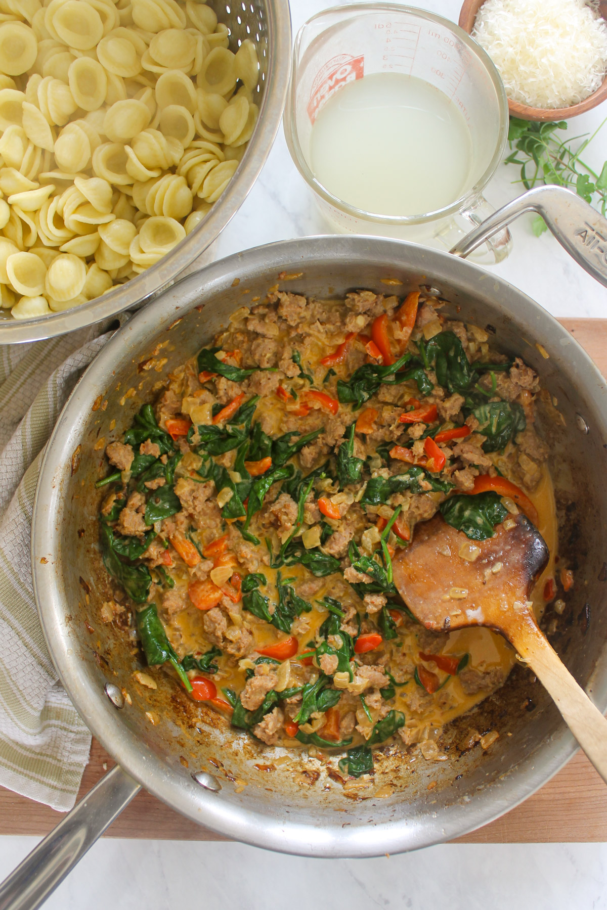 Sausage, pepper and spinach cream sauce with pasta in a colander.