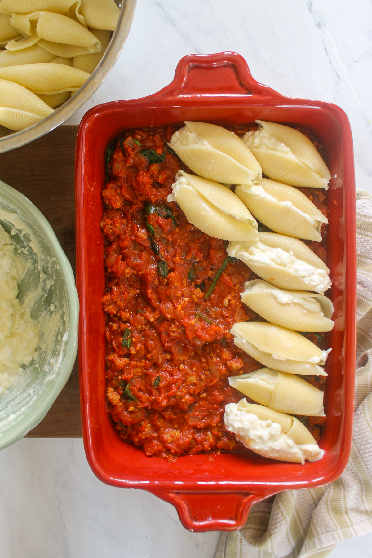 A baking pan of sausage meat sauce with ricotta stuffed shells being assembled.