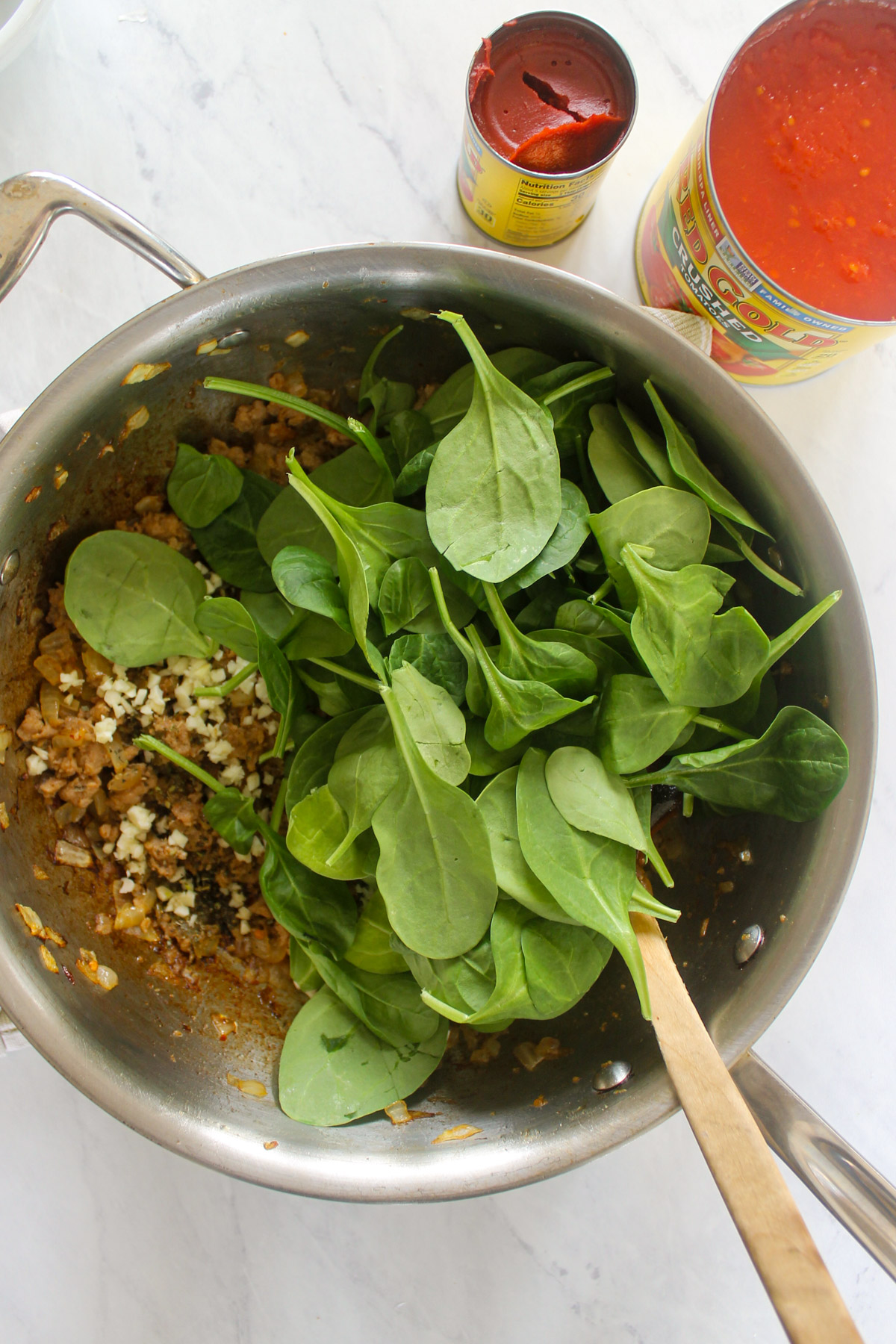 Fresh garlic and spinach added to a skillet of Italian sausage.